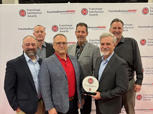 Six men on a red carpet at the Franchisee Satisfaction Awards, one holding the award plate