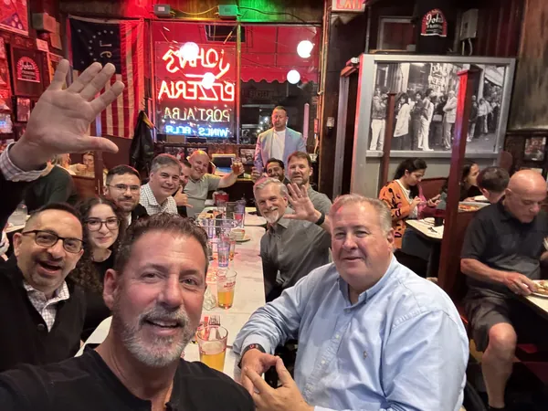 Rob Lancit taking a selfie at a long table of friends inside John's Pizzeria