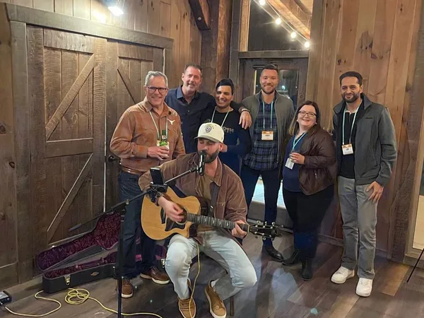 Rob Lancit with friends standing behind a seated guitarist in a wood-paneled room