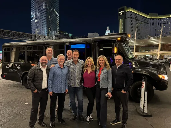 A group of ten in front of a black party bus at night, city lights behind