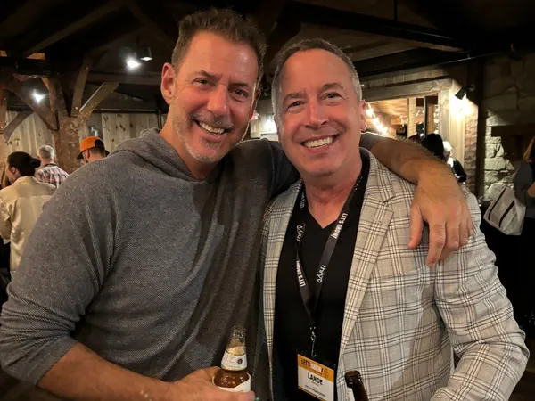 Rob Lancit and a man in a checked blazer holding bottles at an evening event