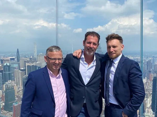 Rob Lancit with two men in suits on a glass observation deck above a city skyline