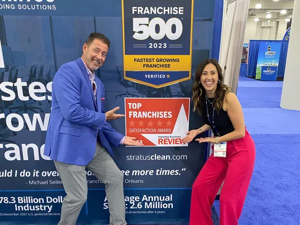 Rob Lancit and a colleague pointing at the Stratus booth wall with the Entrepreneur Franchise 500 2023 banner