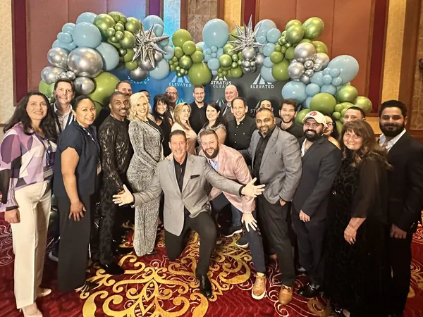 A large group of Stratus franchise owners posing together in a ballroom under a balloon arch