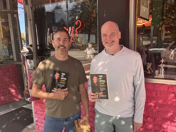 Rob Lancit and a man each holding a copy of Take My Advice, I'm Not Using It outside a restaurant